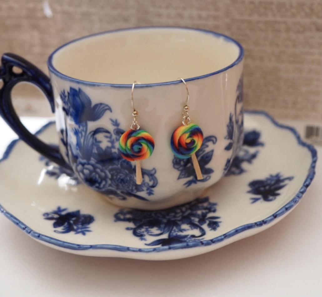 rainbow swirl lolliopop earrings hanging off the side of a teacup